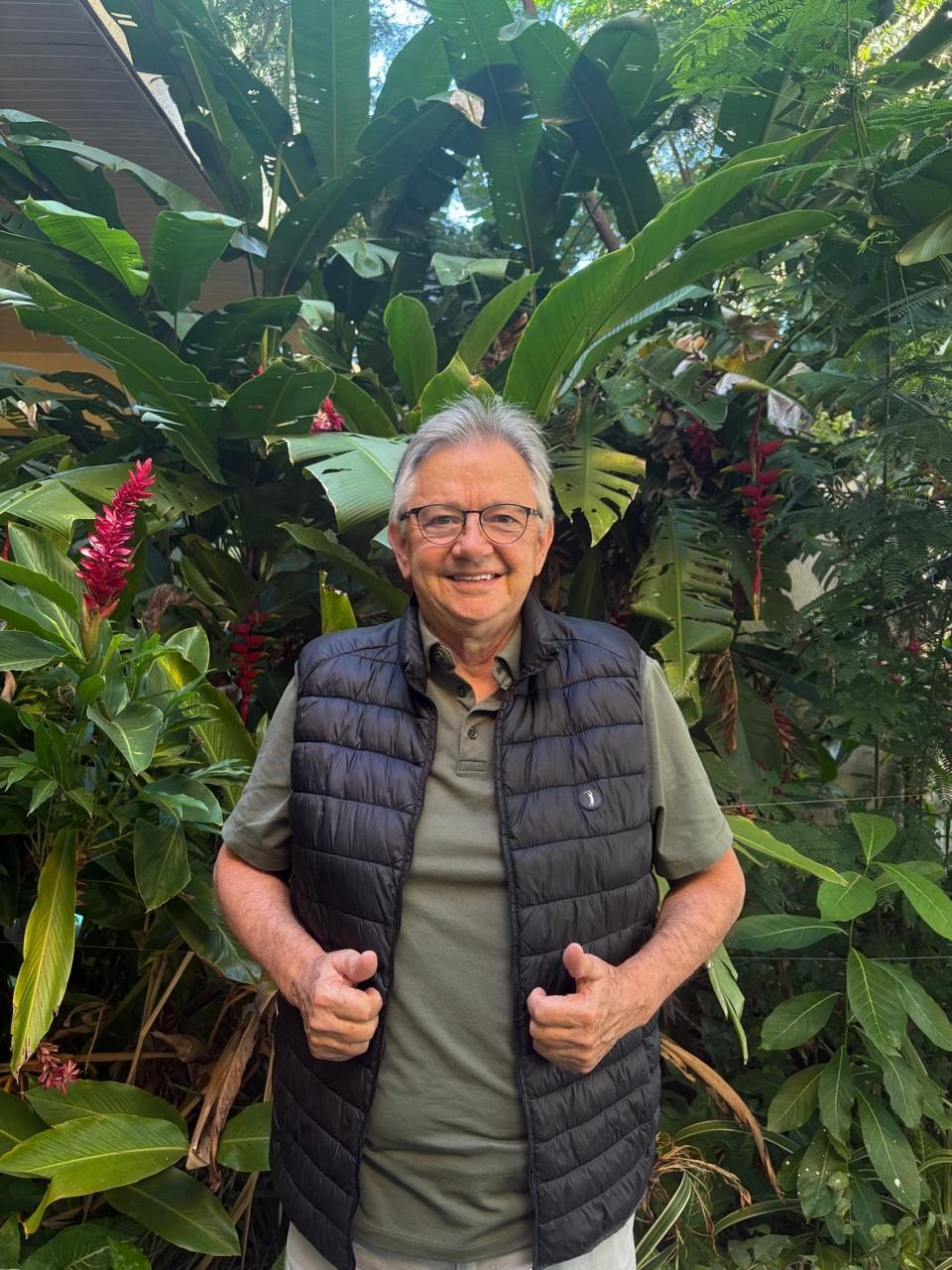 Tarcisio Miguel Sevegnani sorrindo num jardim, entre folhagens e flores